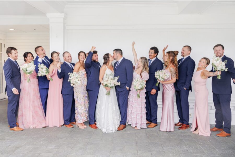 The wedding party cheering as the bride and groom kiss on the covered porch at their Salem Country Club wedding.