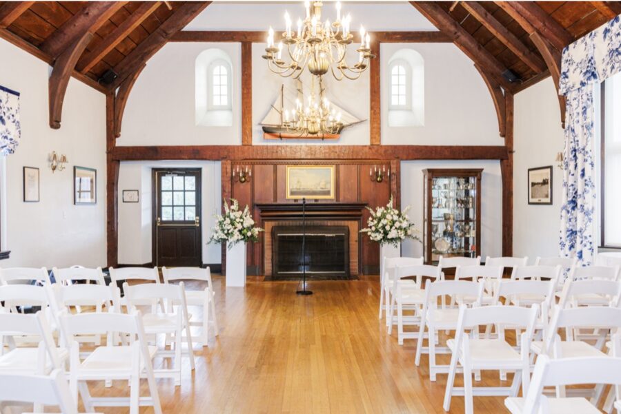 Indoor Salem Country Club wedding ceremony setup with white chairs and flowers flanking the fireplace.