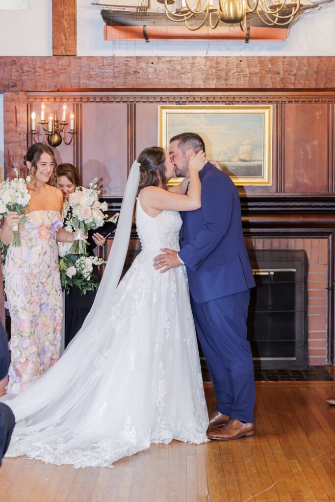 The bride and groom sharing their first kiss in front of the fireplace at their Salem Country Club wedding ceremony.