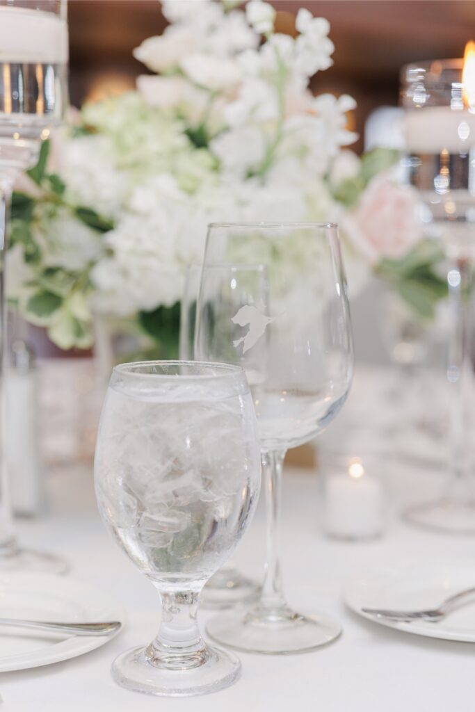 Wine glass etched with the club’s witch emblem beside a water goblet at the Salem Country Club wedding reception.