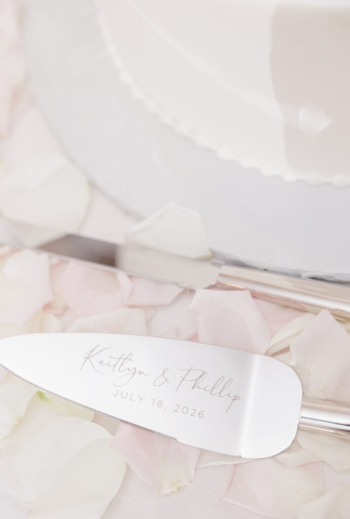 Engraved cake-cutting utensils resting among rose petals beside the Salem Country Club wedding cake.