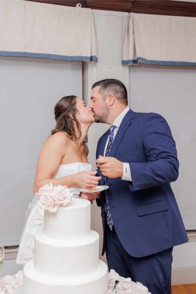 The bride and groom kissing beside their cake after cutting it at their Salem Country Club wedding reception.