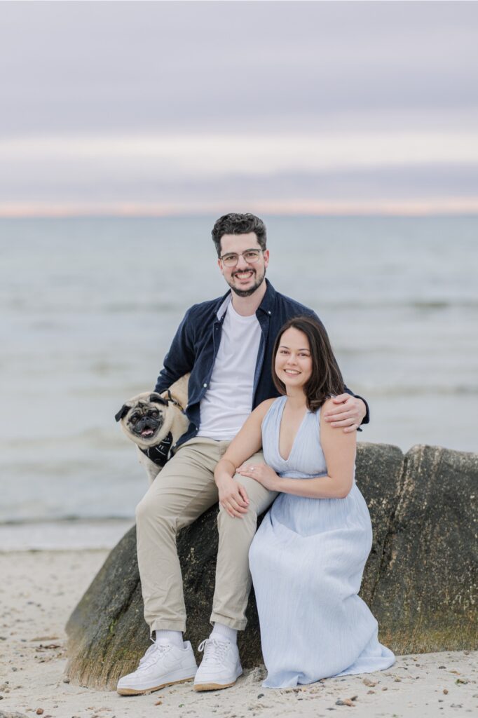Couple posing with their pug on seaside rocks during Cape Cod engagement photos.