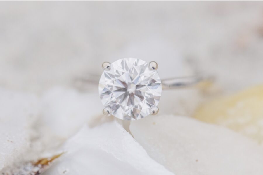 Close-up of a solitaire engagement ring resting on a seashell.
