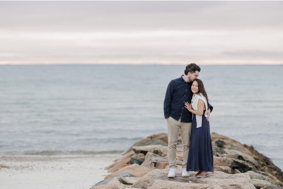 Couple embracing on a rock jetty at sunset during Cape Cod engagement photos.