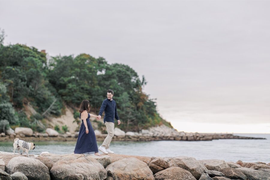 Couple walking hand in hand across seaside rocks with their pug.