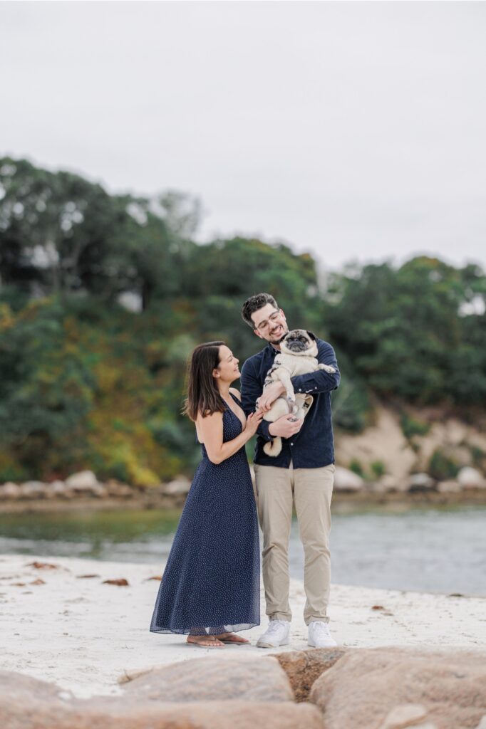 Couple cuddling their pug beside the rocky shoreline at Old Silver Beach.